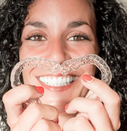 Woman holding two clear dental nightguards in front of her mouth from Night Shield Dental